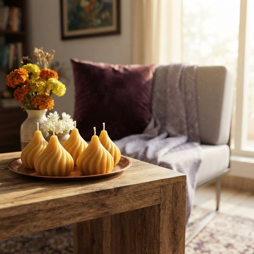 Four modak-shaped scented candles placed on a wooden table in a cozy, traditionally styled Indian living room.